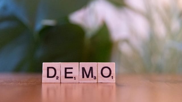 Close-up of wooden letter tiles spelling 'DEMO' on a blurred background, showcasing simplicity.