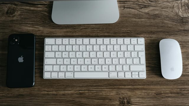 A minimalist workspace featuring a smartphone, keyboard, and mouse on a wooden desk.