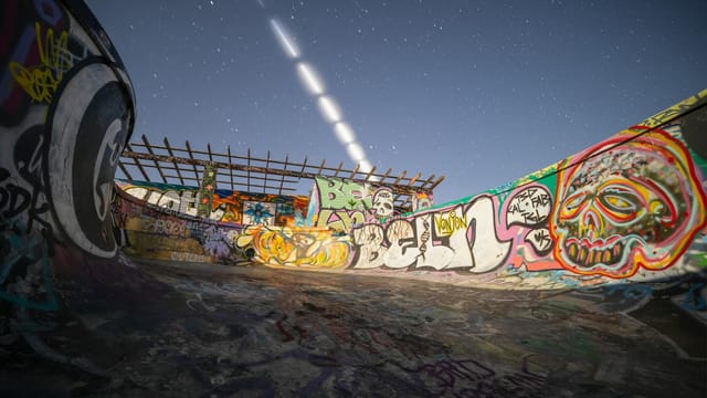 Dynamic view of a graffiti-covered skate park under a starry night sky with light trails.