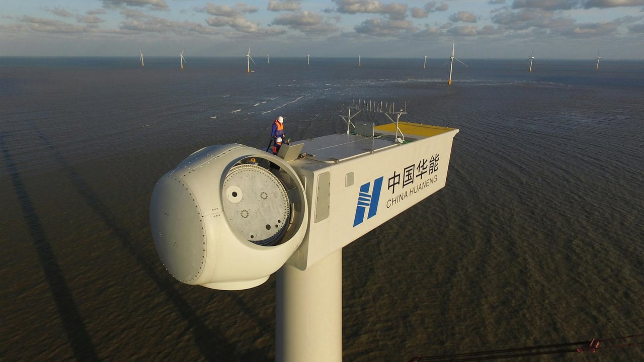 An engineer performs maintenance on an offshore wind turbine, under clear skies.