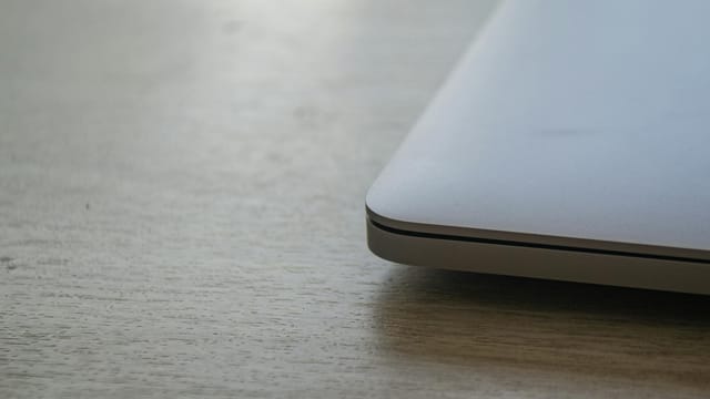 Close up of a sleek modern laptop corner on a wooden desk surface, emphasizing minimalist design.