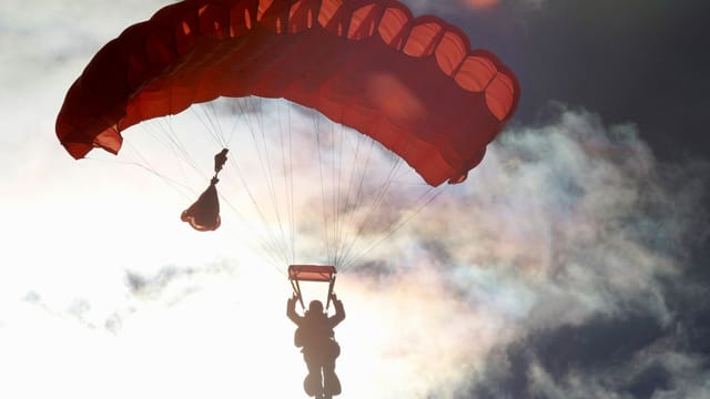 Silhouette of a parachuter descending against a vibrant sunset sky, capturing the thrill of aviation and freedom.