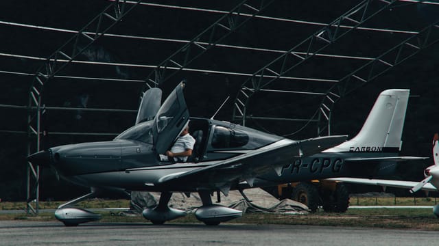 Modern light aircraft parked in an open hangar with visible framework, highlighting transportation.