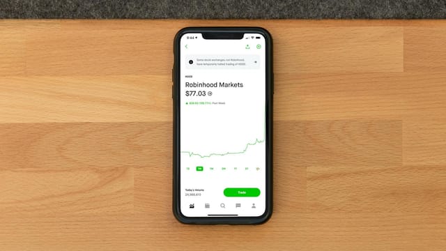 Stock trading app on smartphone displaying Robinhood Markets price on wooden desk.