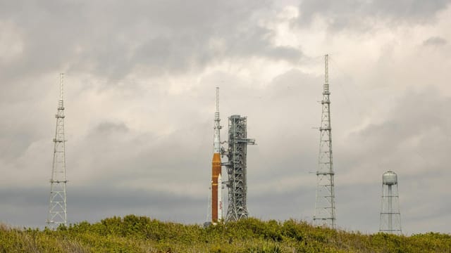 NASA rocket on launch pad surrounded by antennas against a cloudy sky.