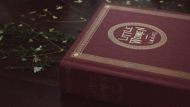 Close-up of a vintage Little Women book with decorative cover on a wooden table.