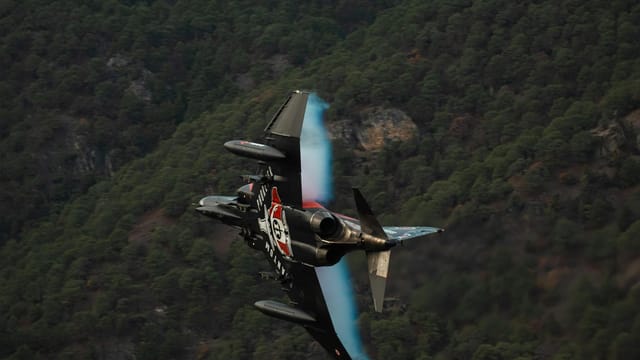 Impressive aerial view of a Turkish Air Force jet maneuvering over forested terrain.