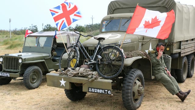 Scene of vintage military vehicles with British and Canadian flags and a bicycle.