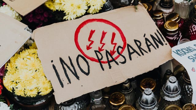 Close-up of protest sign 'No Pasarán' surrounded by flowers and candles.