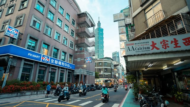 Dynamic Taipei street scene with scooters and the iconic Taipei 101 in the distance.