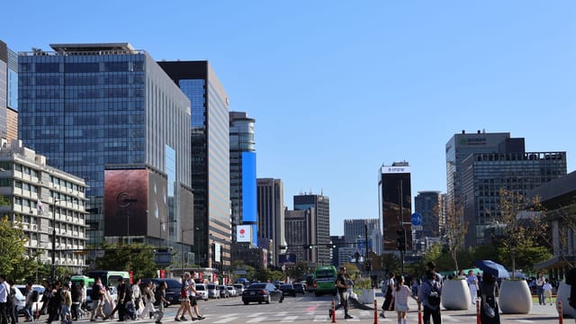 Vibrant street scene in Seoul with skyscrapers and people crossing under a clear blue sky.