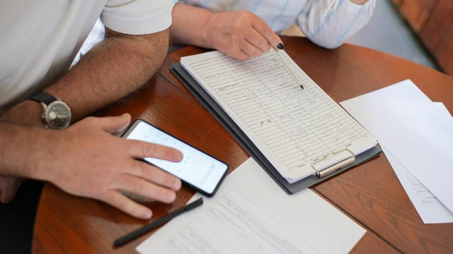 Senior couple examining bills and documents with smartphone and clipboard at home.