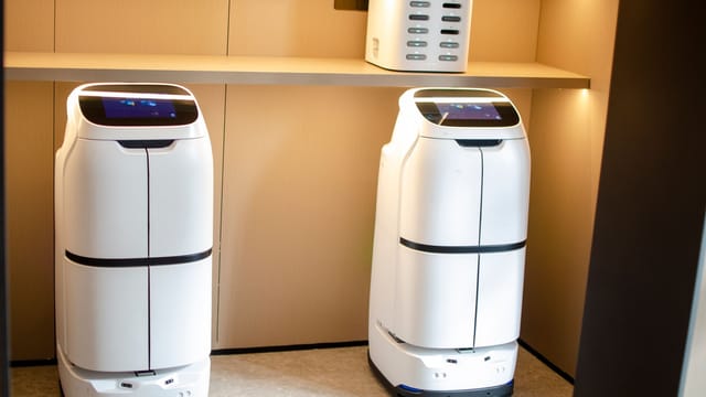 Two white robotic delivery systems located in a modern indoor room with soft lighting.