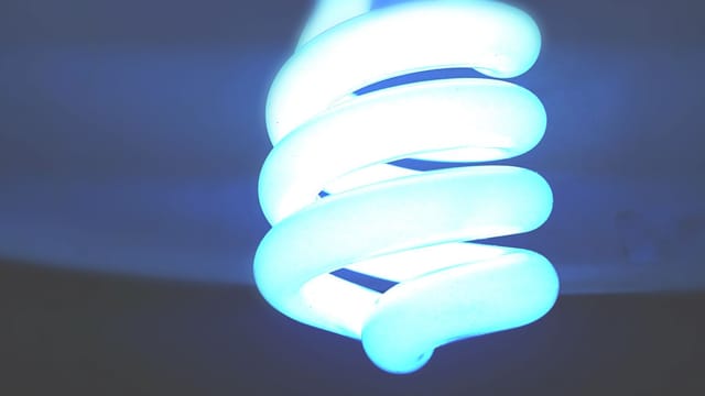 A close-up shot of an illuminated spiral CFL bulb emitting a blue glow, symbolizing energy efficiency.