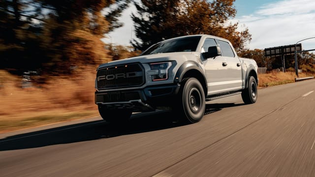 A Ford F-150 driving on a scenic highway surrounded by trees and blue skies.