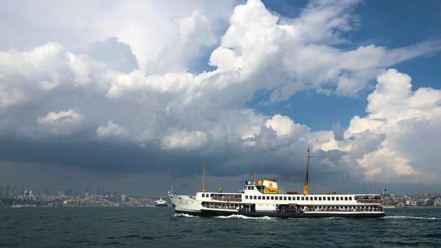 Ferry crossing the Bosporus in Istanbul under dramatic cloudy skies, embodying scenic travel.