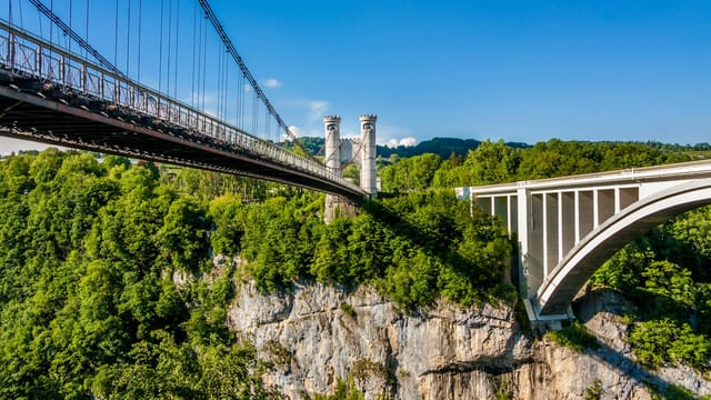 Aerial view of dual bridges spanning a lush green canyon, showcasing architectural contrast.