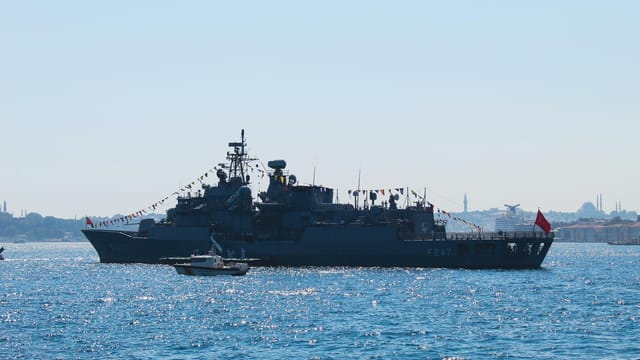 Navy ship on the Bosphorus with Istanbul skyline in background, taken during the day.