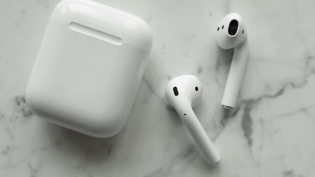 A close-up view of white wireless earbuds and their case on a marble surface.