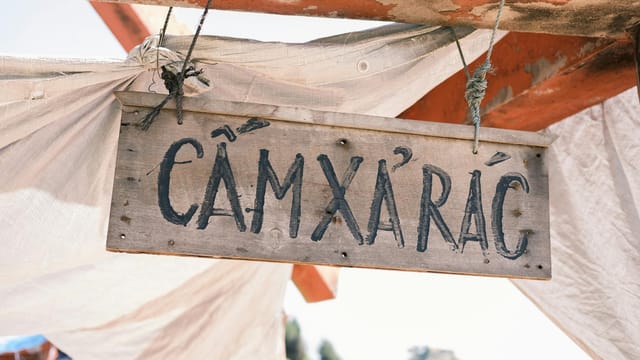 Hanging wooden sign with Vietnamese text outdoors, conveying a rustic and worn appearance.