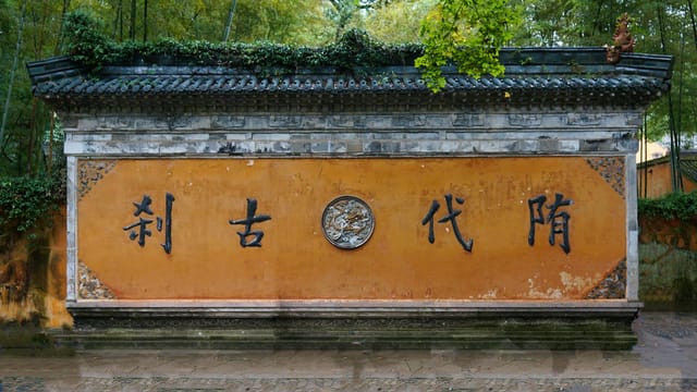 Elegant Chinese wall with intricate characters, surrounded by lush greenery.