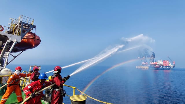 Workers on an offshore platform demonstrate teamwork using water hoses under a clear sky.