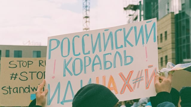 Demonstrators holding anti-Russian signs during a protest in city streets, highlighting political tensions.