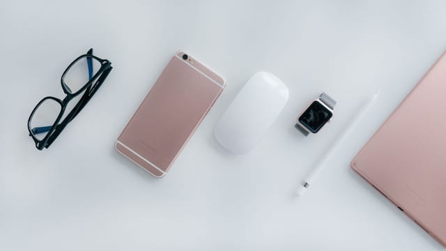 Elegant arrangement of glasses, phone, watch, mouse, pencil, and tablet on a white surface.