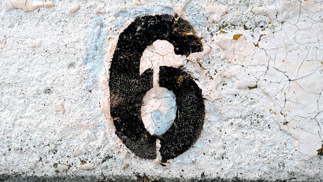 Close-up of a weathered number six painted on a cracked road surface.