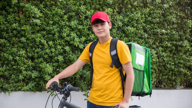 Asian male courier with backpack and bicycle, ready for delivery outdoors.