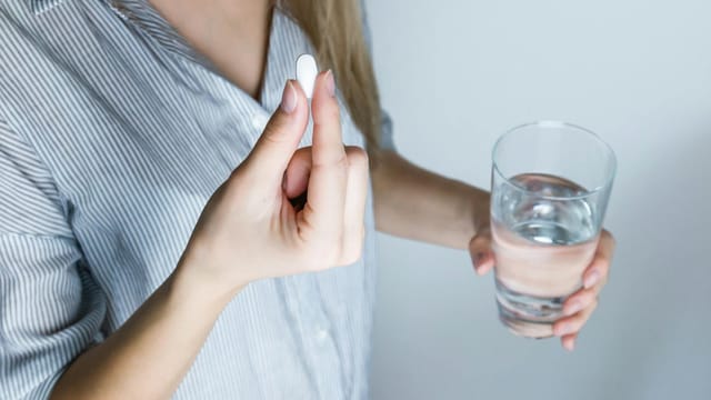 Close-up of a woman holding a pill and a glass of water, ready to take medication.