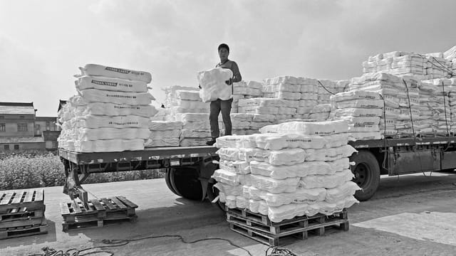 A worker organizes cargo stacks on a truck in an industrial area.