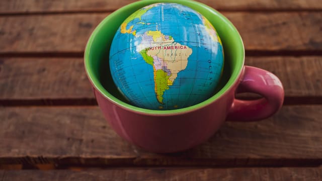 A vibrant globe inside a mug placed on a rustic wooden surface, symbolizing global travel.