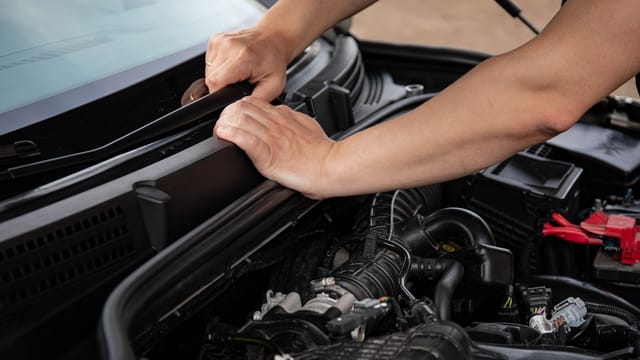 Close-up of hands repairing a car engine outdoors, focusing on automotive maintenance.