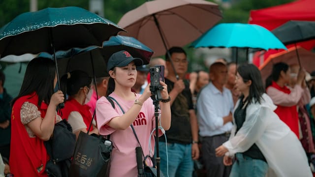 A group of people using smartphones and umbrellas during a rainy event.