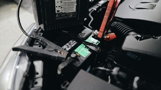 Detailed view of a car battery being jump-started with cables in an engine bay.