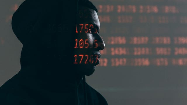 Side profile of a man in a hoodie, surrounded by red code, depicting cybersecurity theme.