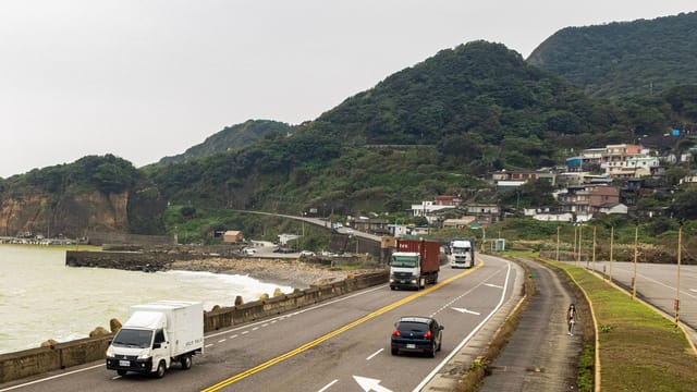 Traffic along a coastal road with trucks and mountains in the background, ideal for transportation themes.