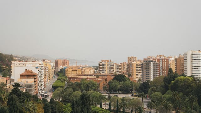 A cityscape with apartment buildings, park, and foggy skyline in Malaga, Spain.