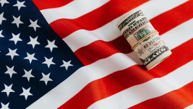 From above of United States currency folded in roll placed on USA flag illustrating concept of business profit and wealth