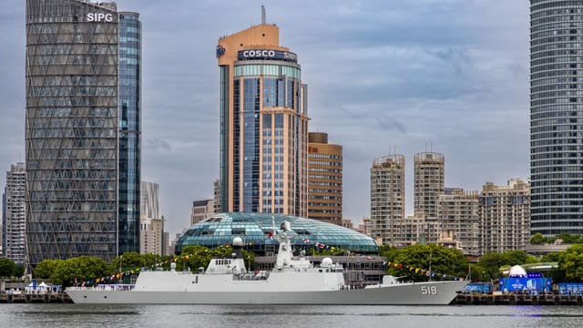 Contemporary skyline of Shanghai with a naval ship anchored, capturing urban architecture and maritime activity.