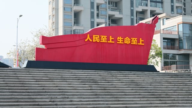 Red sculpture with Chinese text on urban steps, modern buildings backdrop.