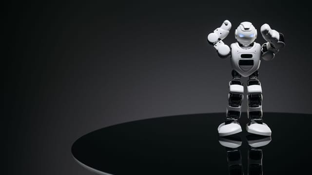 A small humanoid robot with glowing eyes on a reflective table in a dark setting.