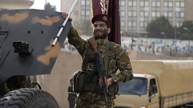 Syrian soldier in a parade in Damascus with military vehicles.