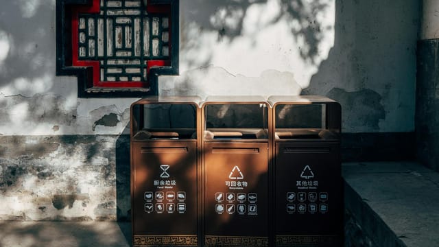 Sunlit traditional Chinese wall and recycling bins in an outdoor setting.