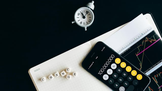Notebook with an iPhone displaying 100,000,000, desk clock and financial charts suggesting market analysis.