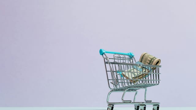 A close-up of a mini shopping cart with rolled cash on a pastel background. Ideal for finance and ecommerce themes.