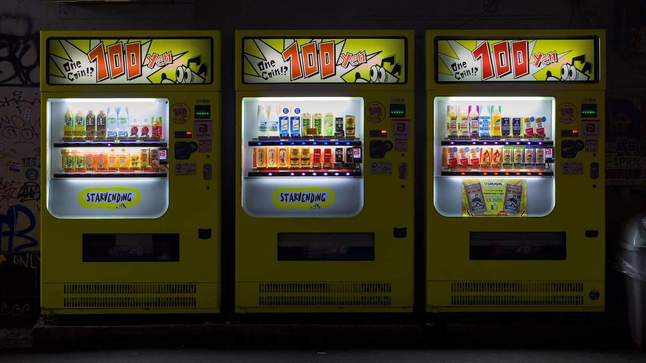 Three brightly lit vending machines on an urban street in Osaka, Japan at night.