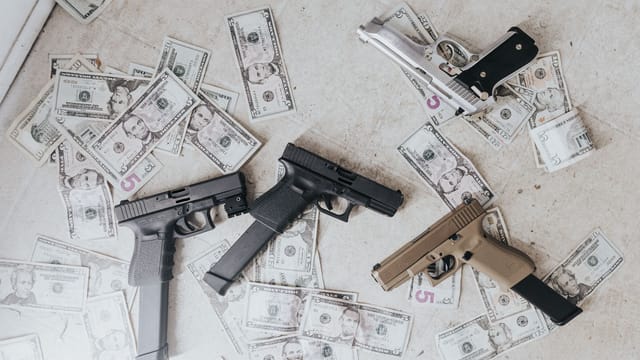Multiple firearms and US dollar bills scattered on a floor in a high-angle view.