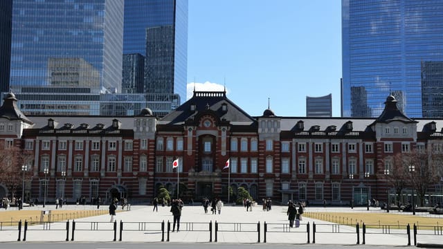 Tokyo Station's historic facade with skyscrapers in the background on a clear day.